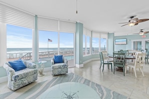A spacious room with large windows, a dining area, and a ceiling fan.