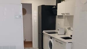 A compact kitchen with a washing machine, a black refrigerator, and a white sink. - THE OLD WINE STATION APARTAMENTS in the very center of the city. (Haro)