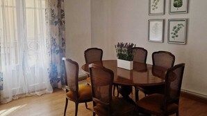 A dining room with a round wooden table surrounded by six wicker chairs, a potted plant, and four framed botanical prints on the wall. - THE OLD WINE STATION APARTAMENTS in the very center of the city. (Haro)