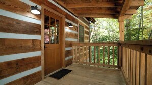 Une cabane en bois dotée d’un porche, de murs en bois et d’une porte avec des panneaux de verre.