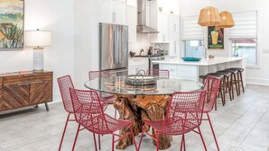 Una cocina moderna con armarios blancos, una isla central y sillas rojas alrededor de una mesa de vidrio.