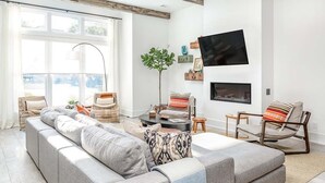 Una sala moderna con un sofá seccional gris, sillas de mimbre, un televisor de pantalla plana y una chimenea.