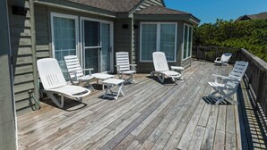 A wooden deck with white lounge chairs and a small table, surrounded by a wooden railing. - Earnest, Ships Watch Community in Duck, NC (Duck)