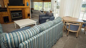 A cozy living room with a fireplace, striped sofa, and a dining table with chairs. - Earnest, Ships Watch Community in Duck, NC (Duck)