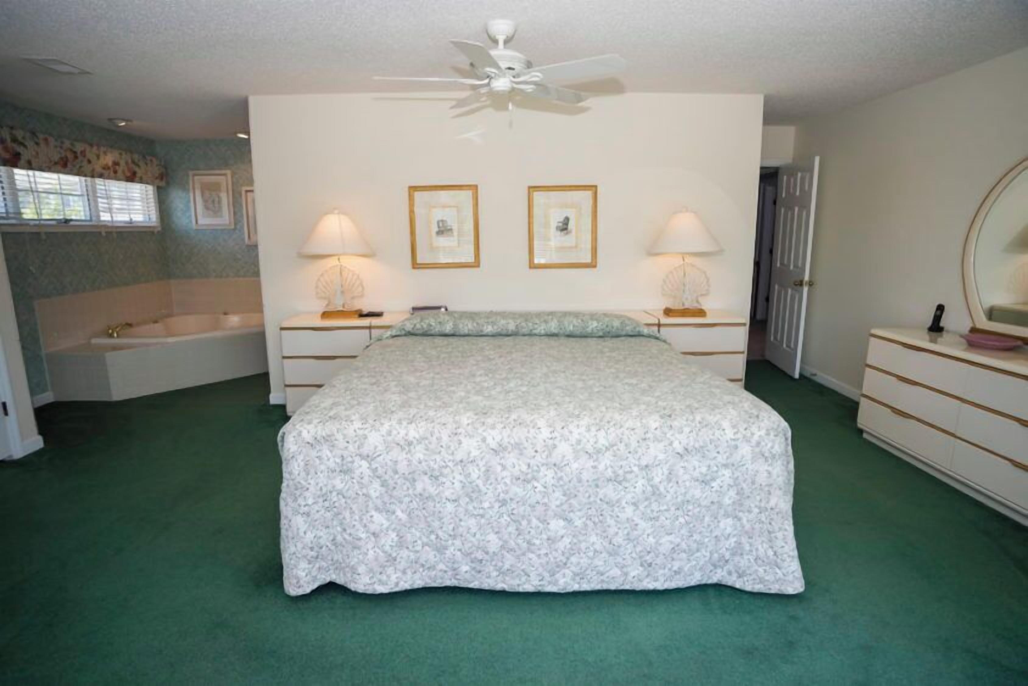 A bedroom with a bed, two bedside lamps, a ceiling fan, a window with blinds, and a door.