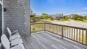 A wooden deck with white chairs, a view of a residential area with houses and trees, and a clear blue sky.