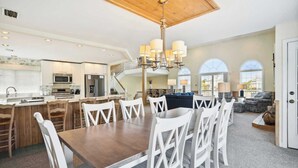 A spacious living area with a dining table, chairs, and a kitchen in the background.