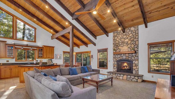 A spacious living area with a stone fireplace, wooden beams, and large windows. - Hot tub, large home, family friendly, ping pong, a premier Sunriver Retreat (Sunriver)