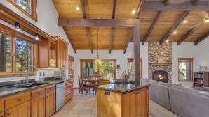 A spacious kitchen with wooden cabinets, a central island, and a stone fireplace. - Hot tub, large home, family friendly, ping pong, a premier Sunriver Retreat (Sunriver)