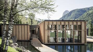 A modern wooden cabin with large windows, a wooden deck, and a reflection in the water.