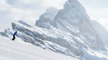 A person skiing down a snow-covered slope with a mountain in the background.