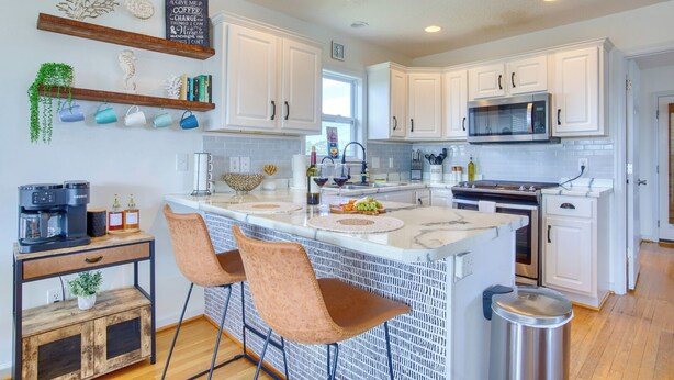 A modern kitchen with white cabinets, a central island with bar seating, a coffee machine, and decorative items. - Welcome to The Palms @ Sneads Ferry, NC! (Sneads Ferry)