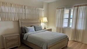 Une chambre à coucher avec un lit, des tables de chevet, une lampe et des rideaux.