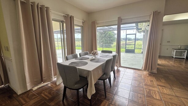 Un coin repas avec une table dressée pour six personnes, de grandes fenêtres avec des rideaux et une vue sur l’extérieur.