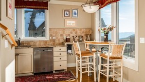 A kitchen with a dishwasher, a dining table with four chairs, and a large window with a view of mountains. - Saddle Ridge F5 3 Bedroom Home (Gallatin Gateway)