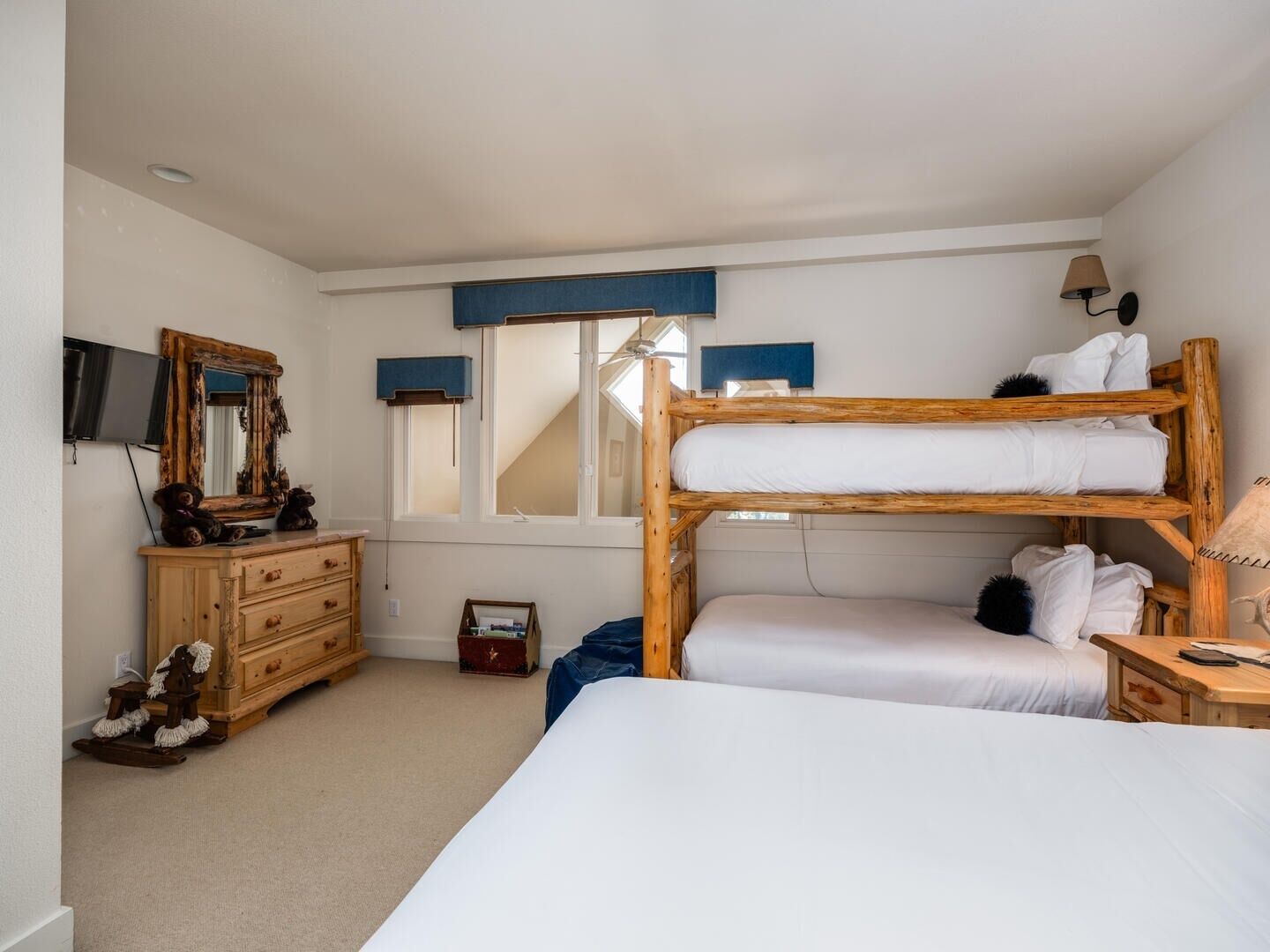 A bedroom with bunk beds, a dresser, a mirror, a television, and a window with blinds.