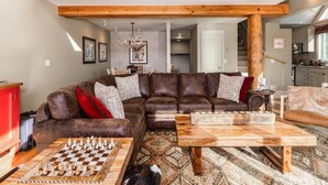 A spacious living room with a large sectional sofa, a wooden coffee table, and a chessboard. - Saddle Ridge F5 3 Bedroom Home (Gallatin Gateway)