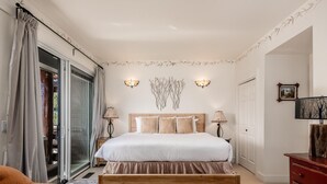 A bedroom with a wooden bed, two bedside lamps, a large window with curtains, a wooden dresser, and a small rug. - Saddle Ridge F5 3 Bedroom Home (Gallatin Gateway)