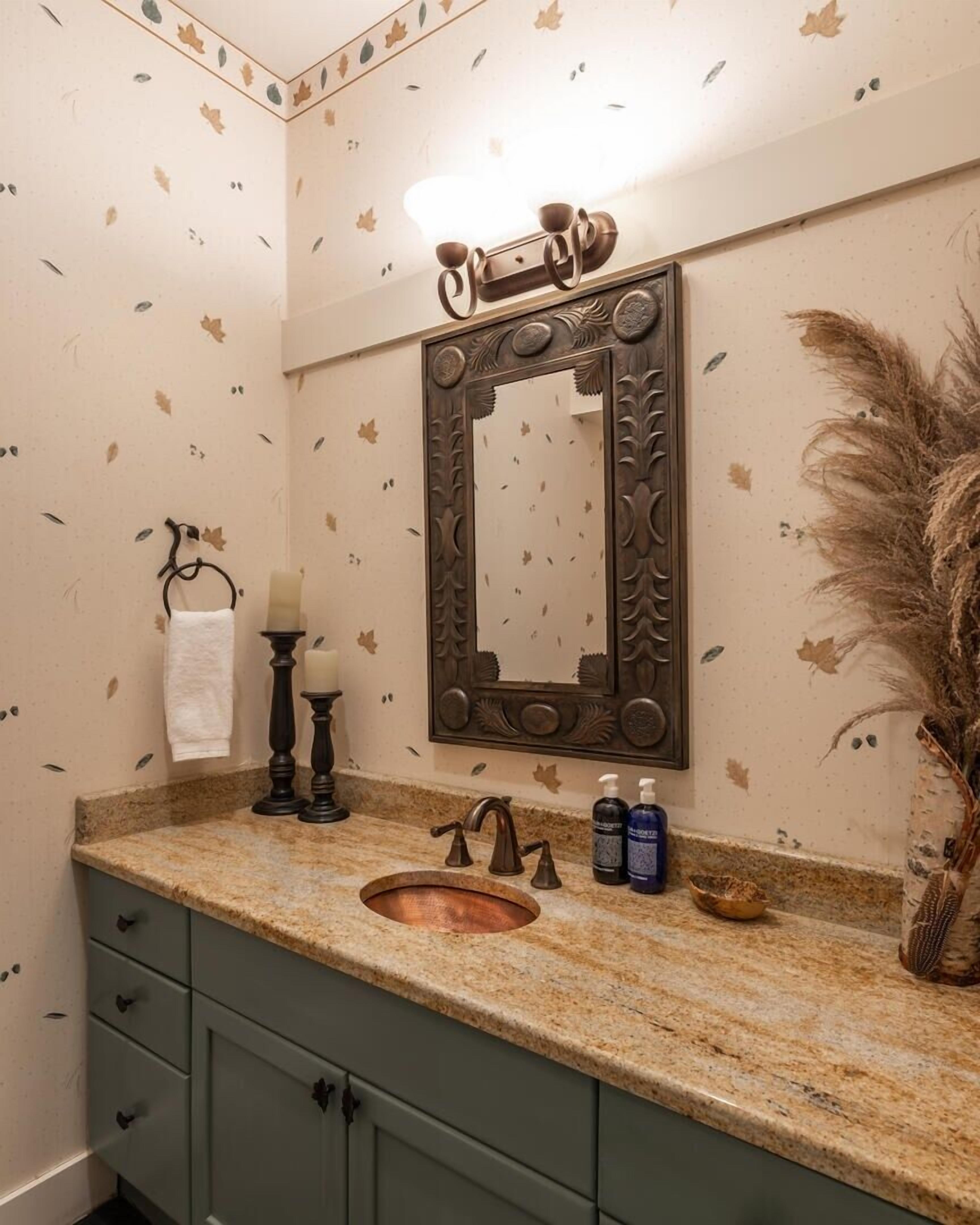 A bathroom with a copper sink, a mirror with ornate frame, a candle holder, and toiletries on the counter.