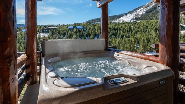 A hot tub with a control panel, surrounded by wooden beams, overlooking a snowy mountain and forested area. - Saddle Ridge F5 3 Bedroom Home (Gallatin Gateway)