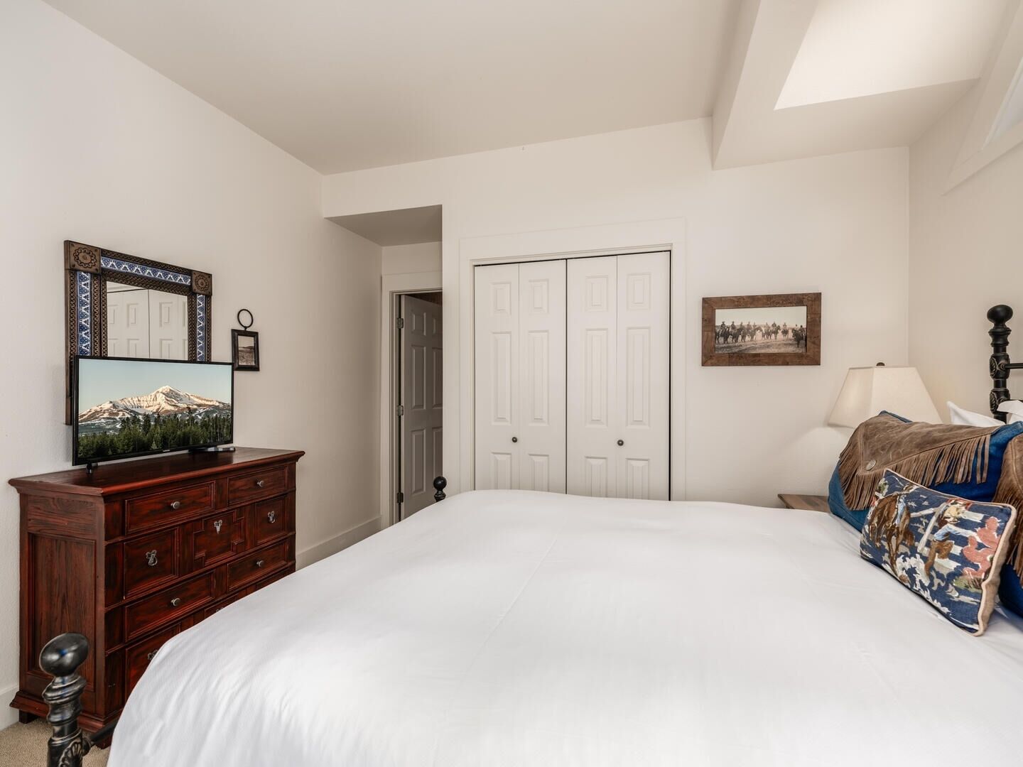 A bedroom with a large bed, a dresser, a television, a door, and a framed picture on the wall.