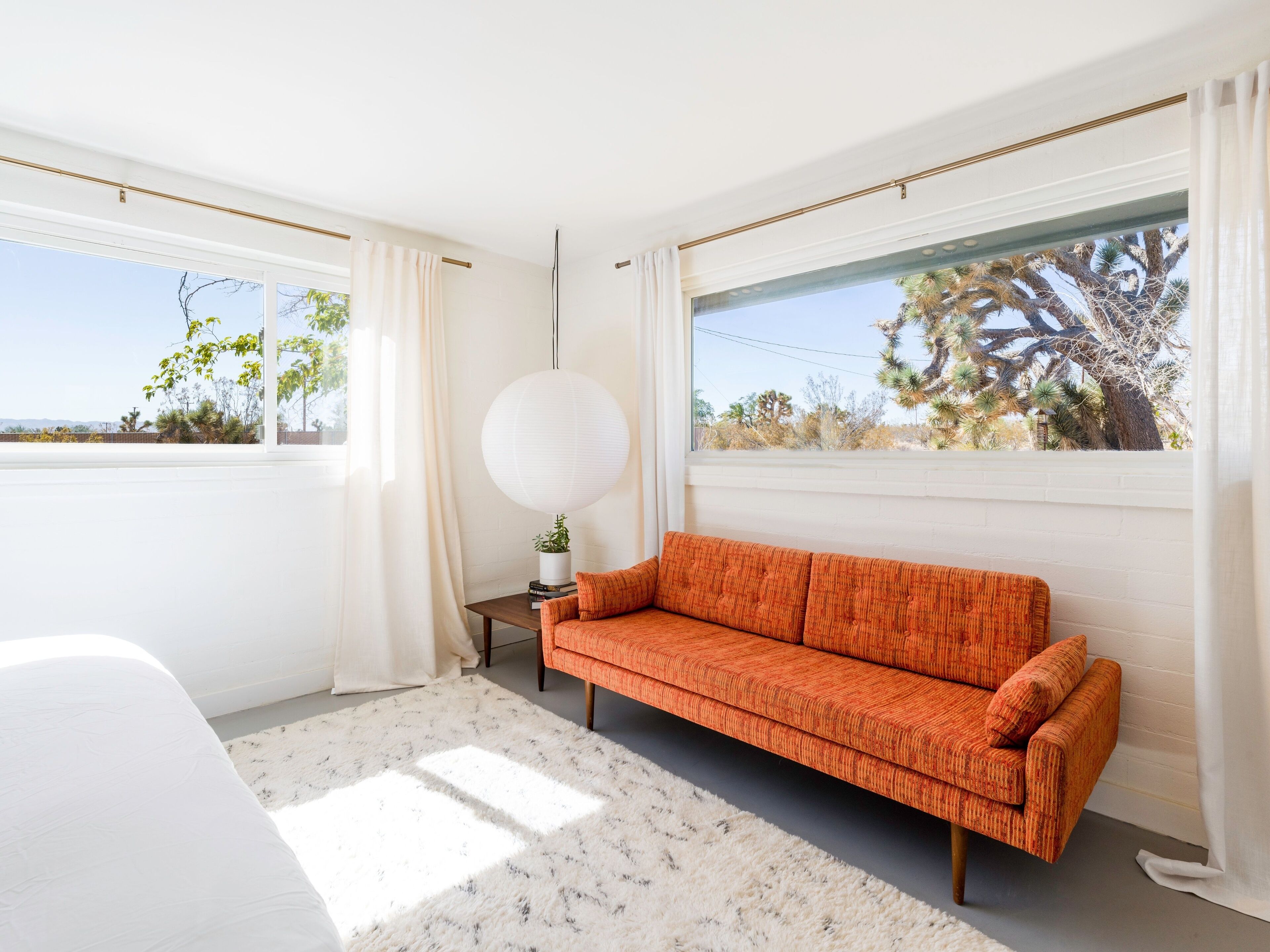 A modern room with a white sofa, a round table with a plant, and large windows with a view of desert vegetation.