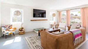 Ein modernes Wohnzimmer mit weißer Ziegelwand, einem Wand-Fernseher, einer Couch, einem Couchtisch und Blick ins Freie.
