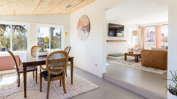 Ein modernes Wohnzimmer mit Essbereich, ausgestattet mit Holzboden, weißen Backsteinwänden und großen Fenstern.