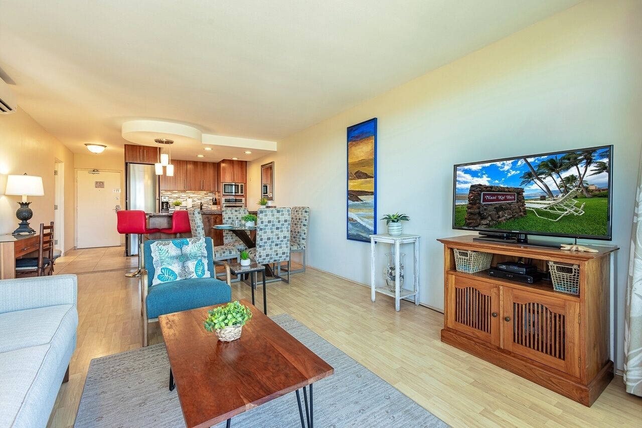 A modern living room with a TV, a dining area, and a kitchen.