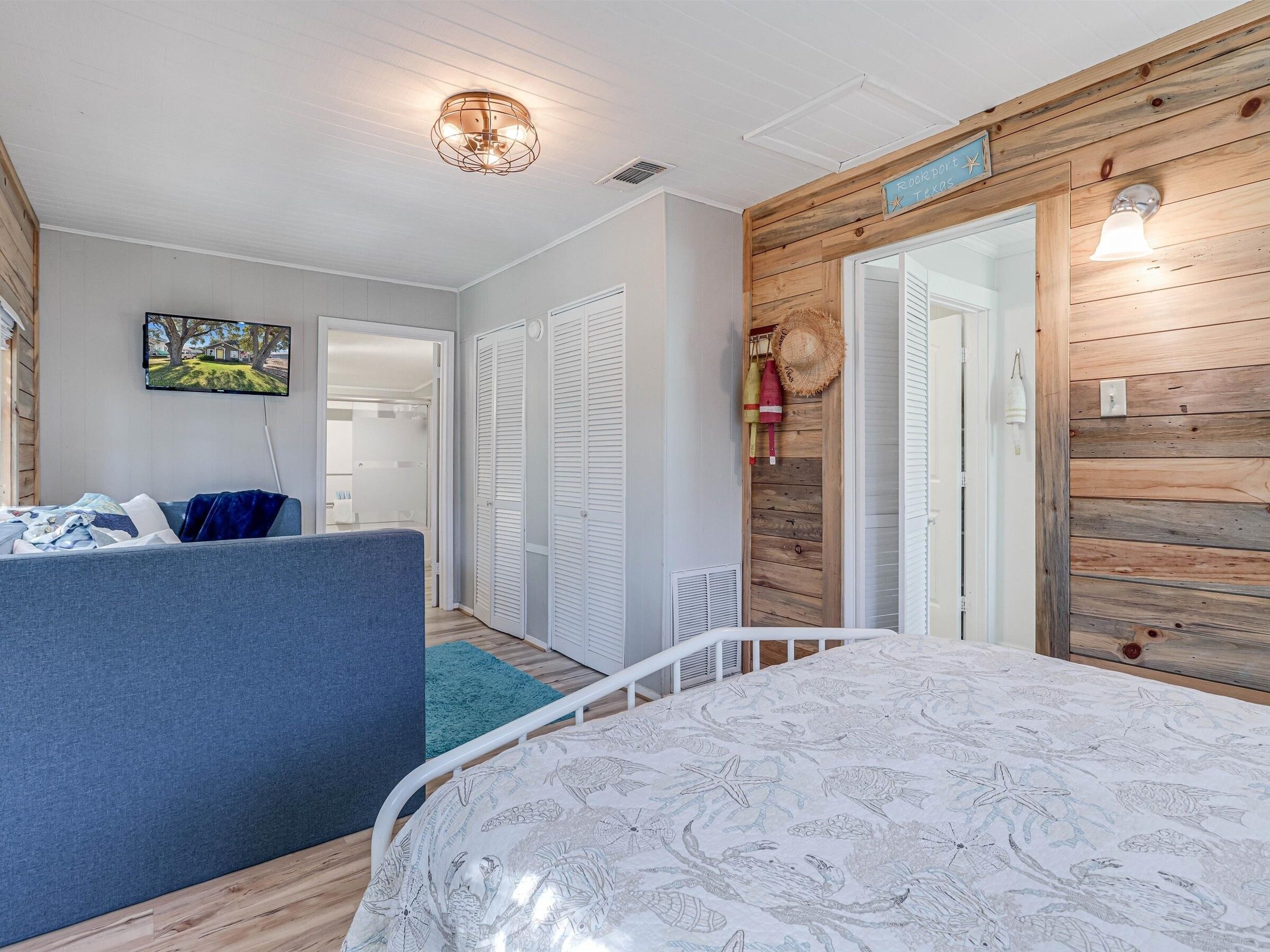 Une chambre à coucher avec un lit, un canapé bleu, un téléviseur et un mur en bois sur lequel est affiché un panneau indiquant « Rockport, Texas ».
