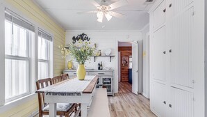 A dining area with a wooden table, chairs, and a bench. There is a ceiling fan, a vase with flowers, and a wall sign that says "gather".