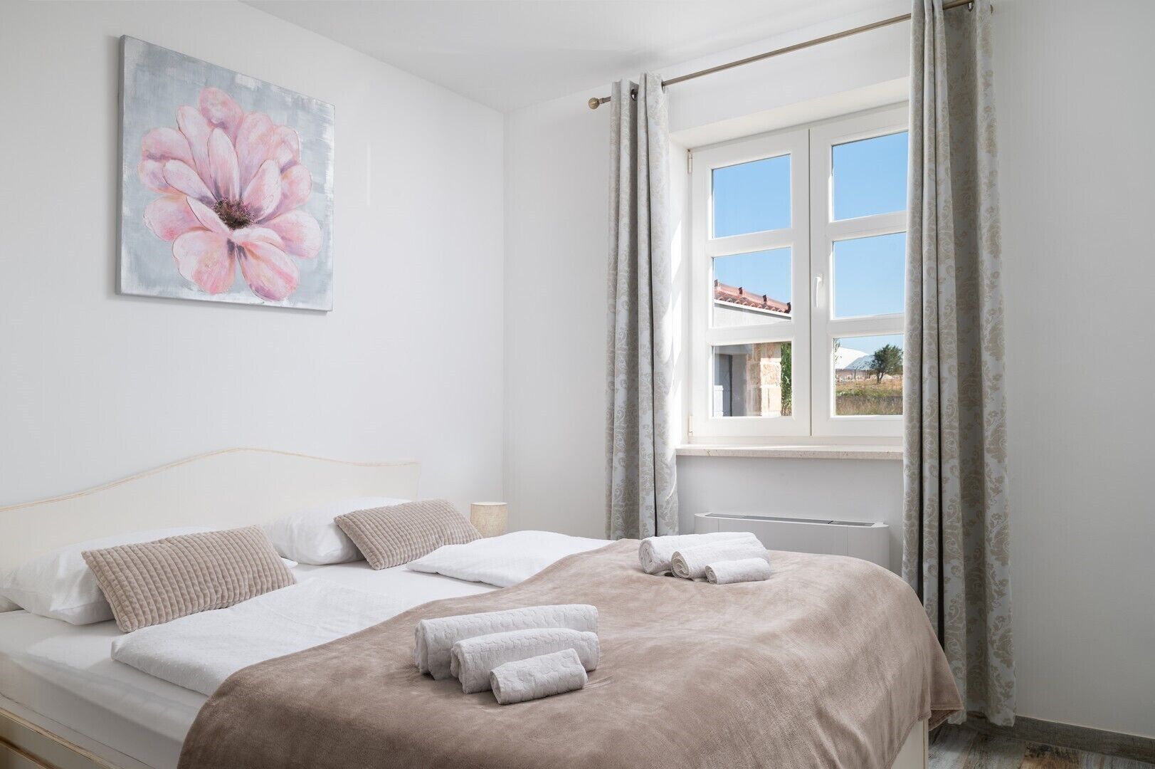Una camera da letto con un letto, due cuscini, una coperta e un quadro di un fiore appeso al muro.