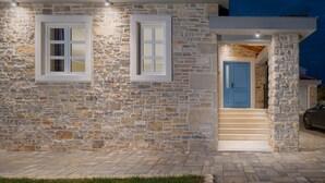 A stone house with a blue door, a staircase leading to the entrance, and a paved driveway.