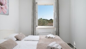 A bedroom with a bed, pillows, a blanket, and rolled towels.