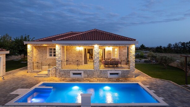 A stone house with a tiled roof, a swimming pool, and outdoor lighting.