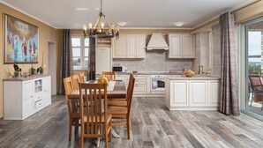 A modern kitchen with a dining area, featuring wooden flooring, white cabinetry, and a large window.