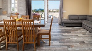 A dining area with wooden chairs and a table, a gray sofa, and a view of the outdoors through a glass door.