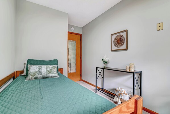 Une chambre à coucher avec une couvre-lit matelassé vert, une tête de lit en bois, une table de chevet ornée d’un vase de fleurs et une œuvre d’art encadrée accrochée au mur.