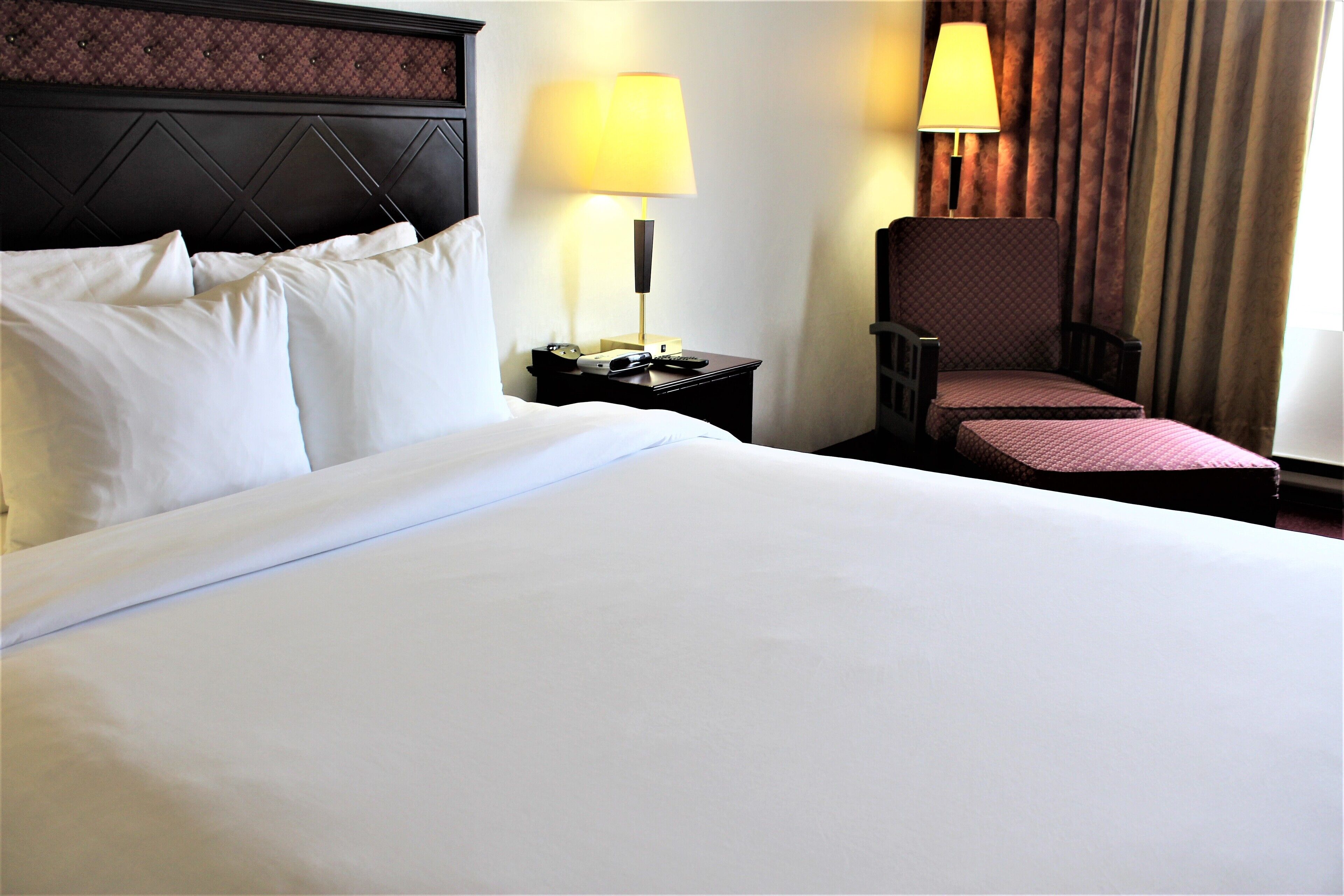Hotelkamer met een groot bed, twee bedlampen, een nachtkastje, een stoel en een raam met gordijnen.