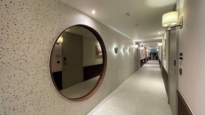 A hotel hallway with a speckled floor, a round mirror, and doors with room numbers.