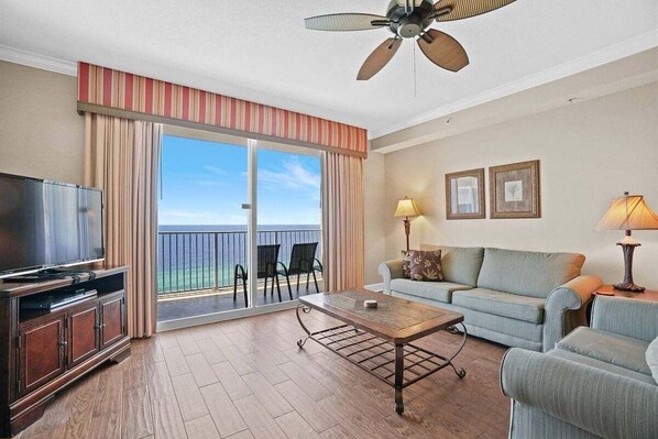 A hotel room with a balcony, a television, a sofa, a coffee table, and a ceiling fan.