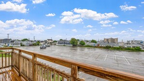 Une vue depuis un balcon en bois donnant sur un parking, avec plusieurs bâtiments en arrière-plan.
