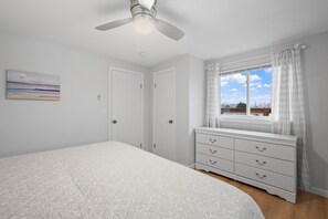 A bedroom with a bed, a dresser, a ceiling fan, and a window with curtains. - Charming, updated 2-bedroom home, 5 min walk to beach, pets ok, onsite parking! (Hampton)