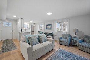 A modern living room with a sofa, two armchairs, a dining table, and a kitchen area. - Charming, updated 2-bedroom home, 5 min walk to beach, pets ok, onsite parking! (Hampton)