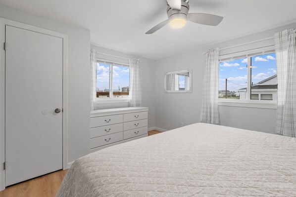A bedroom with a bed, a dresser, a ceiling fan, and two windows with curtains. - Charming, updated 2-bedroom home, 5 min walk to beach, pets ok, onsite parking! (Hampton)