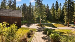 A wooden cabin with a paved driveway leading to a forested area. - Enchanting Home|Hot Tub|Fireplace|12m to Resort (Big Sky)