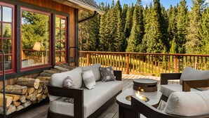 A deck with a sofa and chairs, a fire pit, and a view of a forest. - Enchanting Home|Hot Tub|Fireplace|12m to Resort (Big Sky)