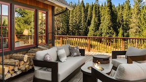 Una terraza con sofá y sillones, un brasero y vistas a un bosque.