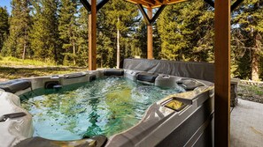 A hot tub with a wooden pergola structure, surrounded by a forested area. - Enchanting Home|Hot Tub|Fireplace|12m to Resort (Big Sky)