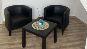 A room with two black armchairs, a small table with a blue bottle, and a staircase with a black railing. - At 100 mt from the sea and train station, rooms with all amenities (Nettuno)